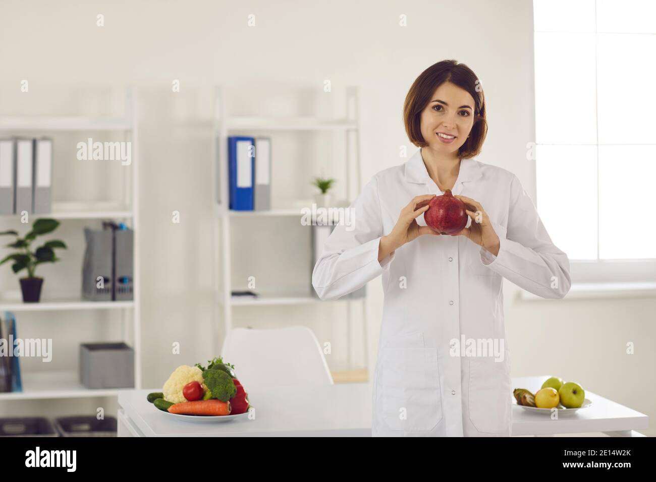 Portrait of a female nutritionist holding a pomegranate in her hands while standing in her office. Stock Photo