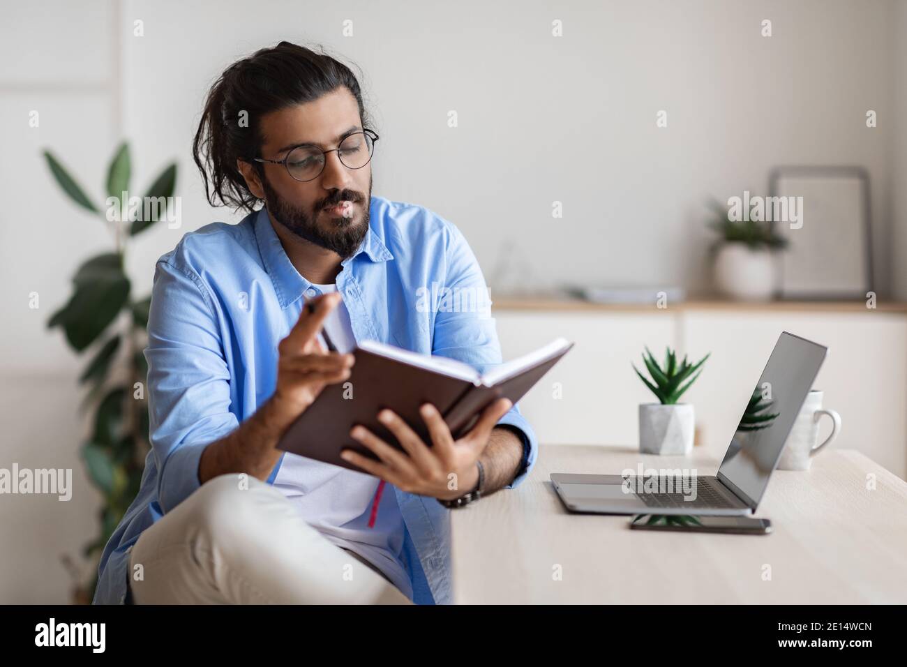 Young Arab Freelancer Guy Checking Working Schedule In Notepad At Home Stock Photo