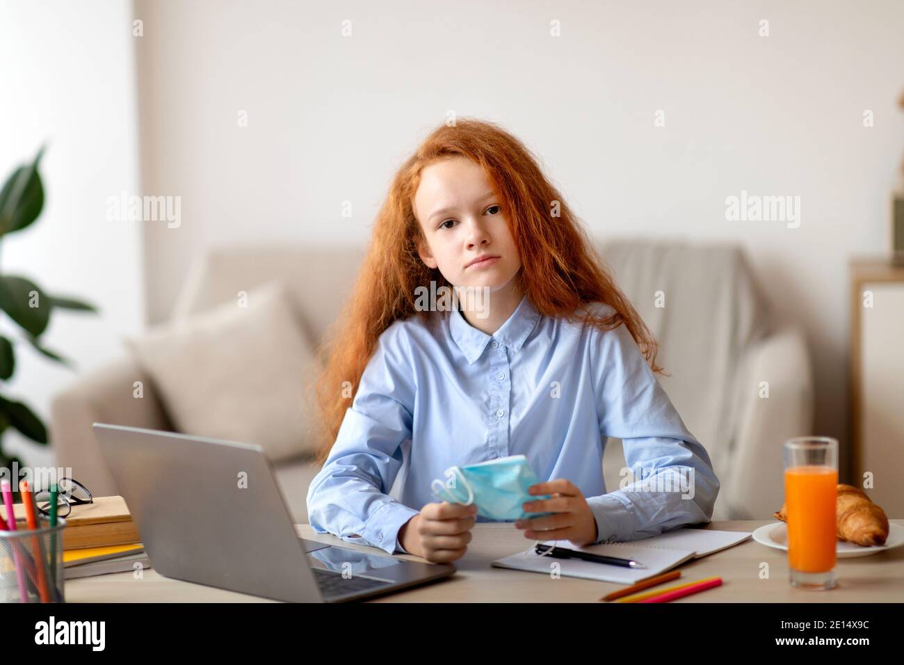 Sad girl holding medical mask studying at home with computer Stock Photo