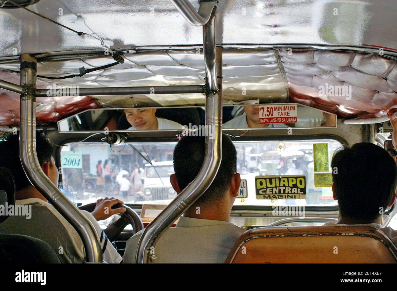 A jeepney driver and two front seat passengers makes their way along the Quiapo Central Mabini route in Manila, Philippines.  The interior shot is taken from the main passenger cabin of this Filipino cultural icon. Stock Photo