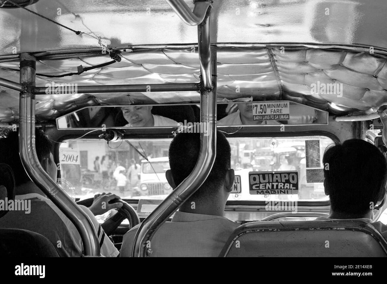 Three men, including the driver, sit in the front seat of a jeepney in Manila, the Philippines.  The interior photo from 2005 shows the destination placard stating the route of Quiapo Central Mabini.  The iconic mass mode of transportation has become a cultural icon of the Philippines. Stock Photo