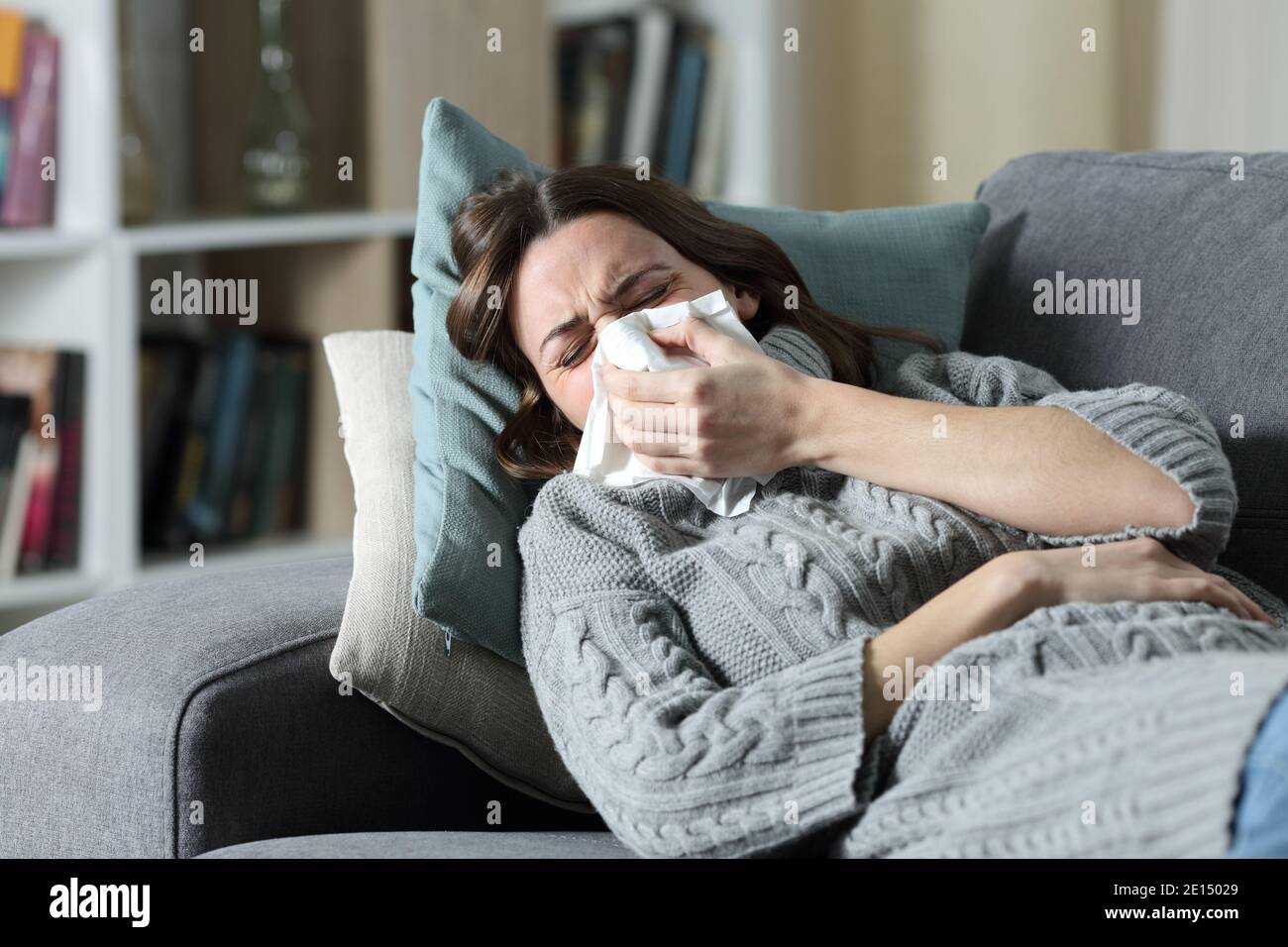 Ill woman suffering flu symptoms blowing on tissue lying on a couch at home Stock Photo