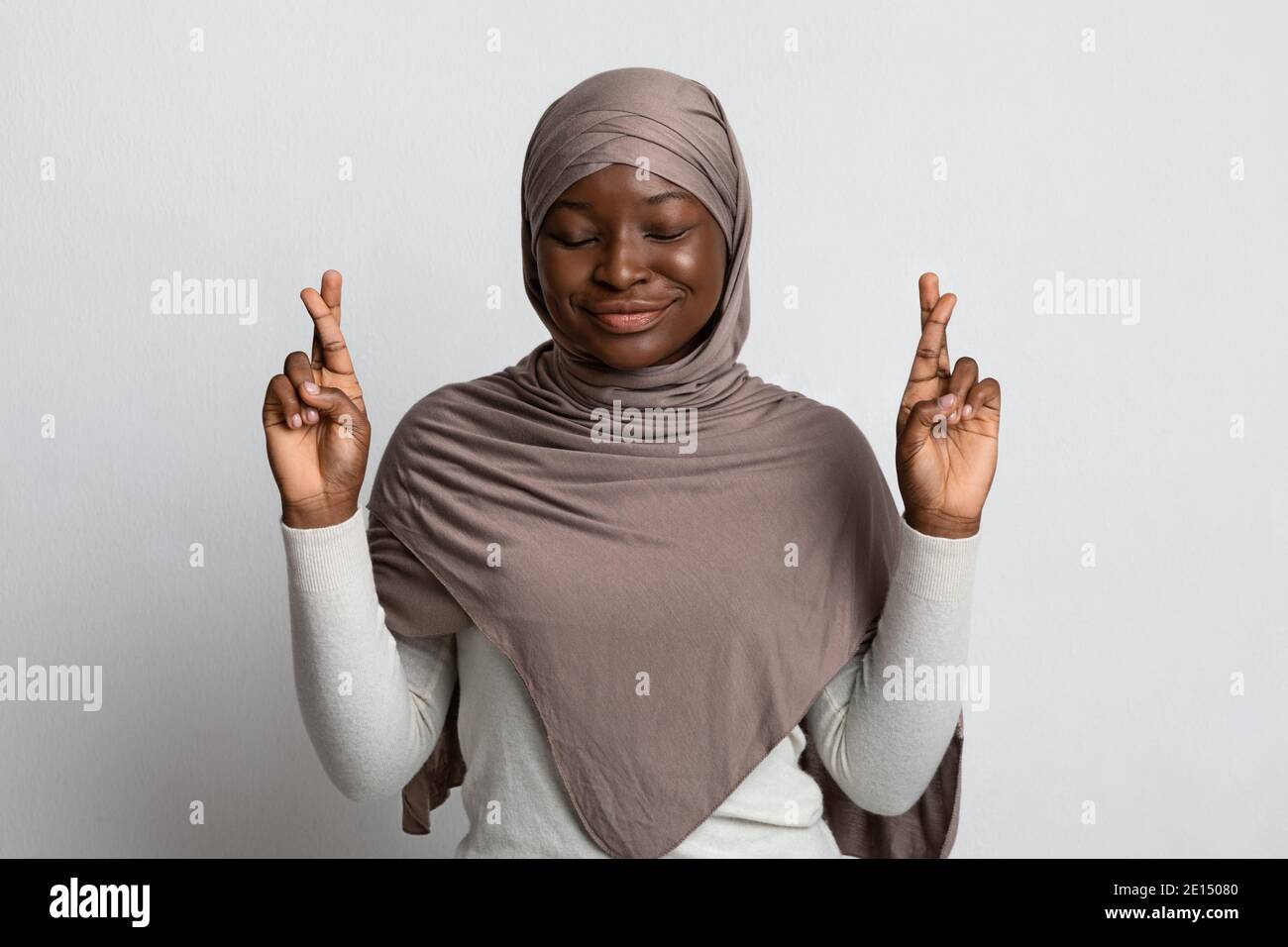 Superstitious Black Muslim Woman In Hijab Making Wish With Crossed Fingers Stock Photo