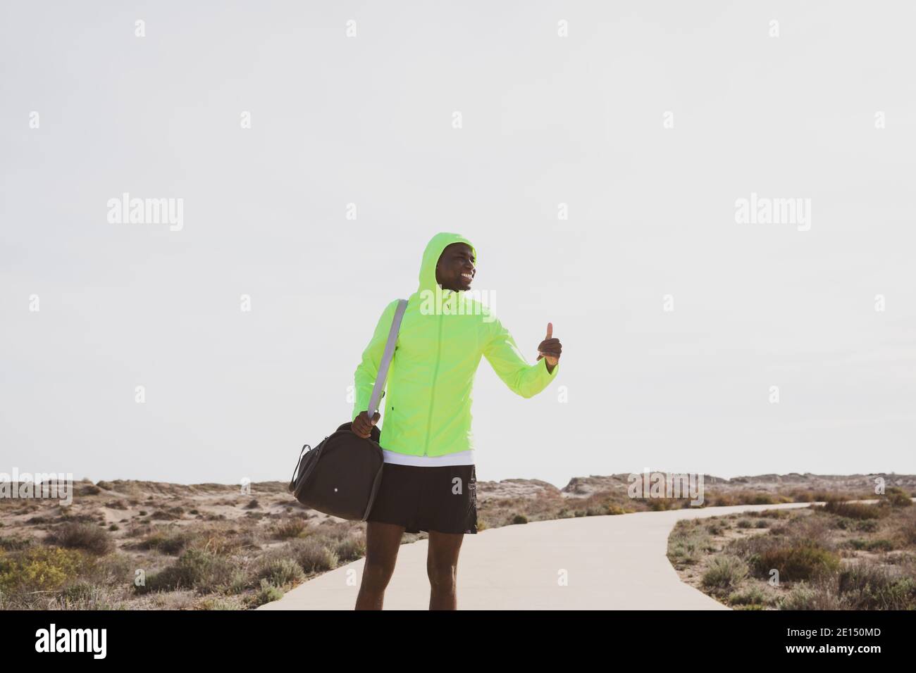 Young black runner with bag and yellow rain jacket who waves as he arrives to train. Stock Photo