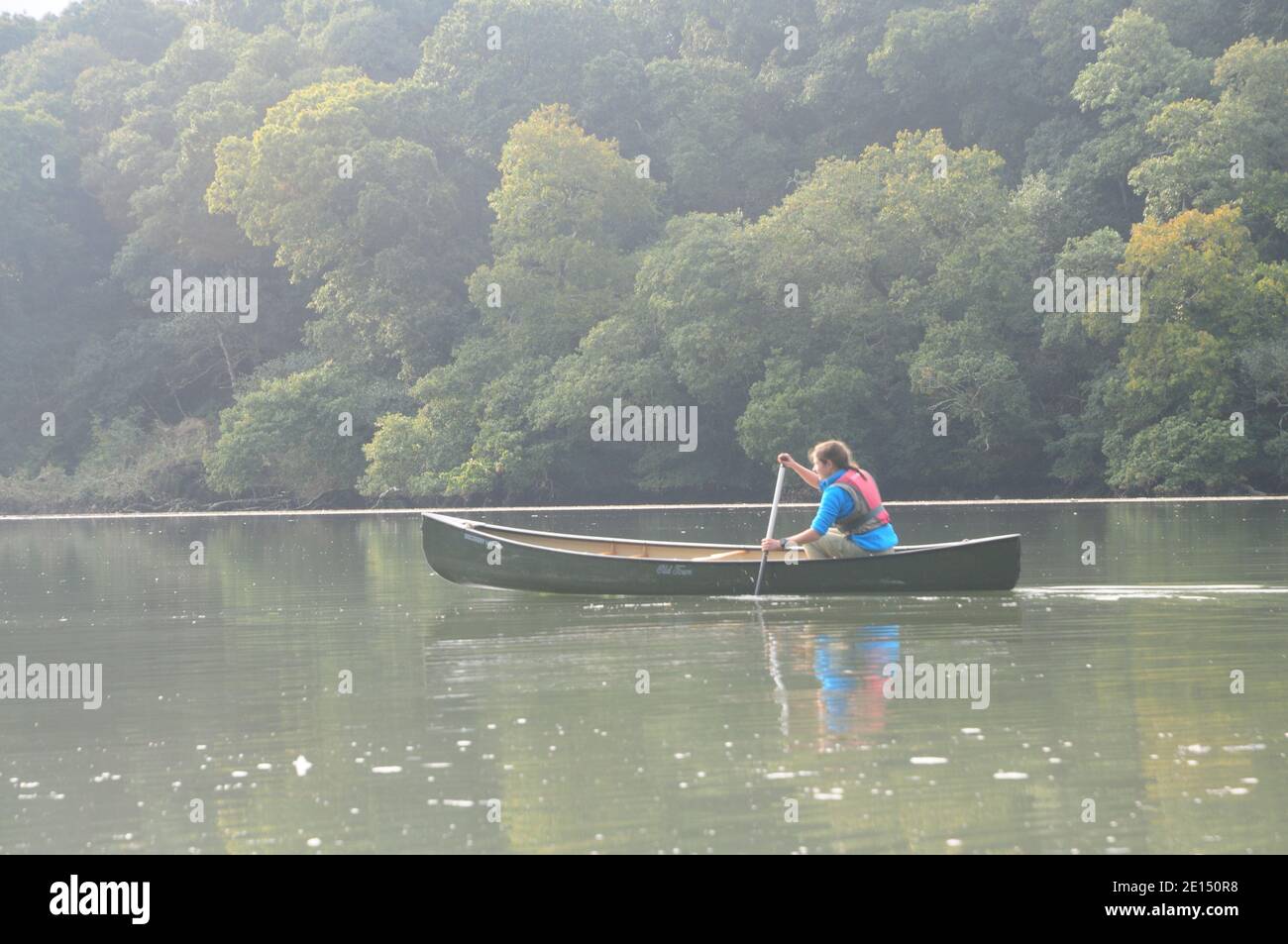 Young lady paddling a Canadian canoe in calm water on a Cornish estuary Stock Photo