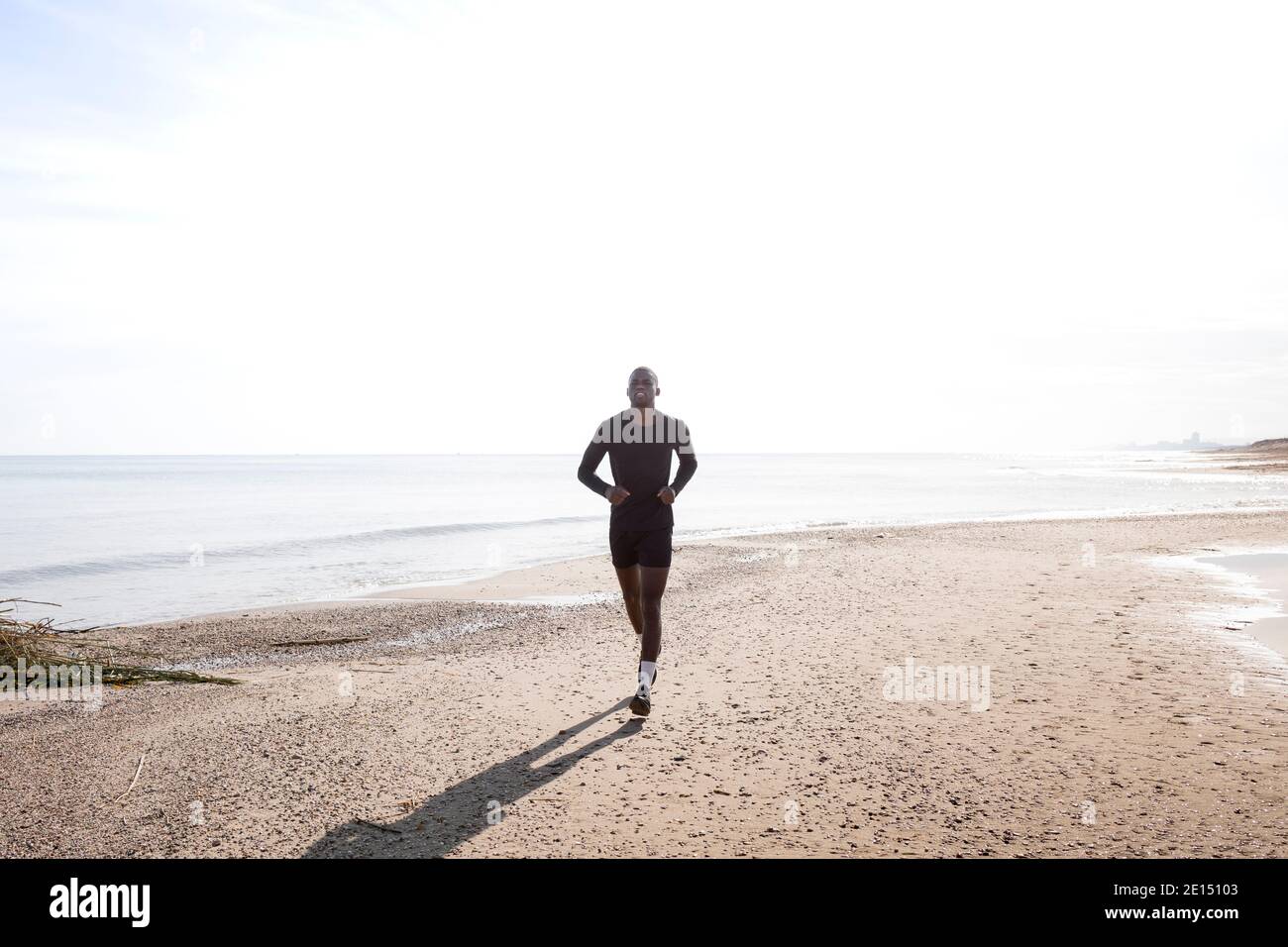 Black sportsman who practices running on the beach with a back light