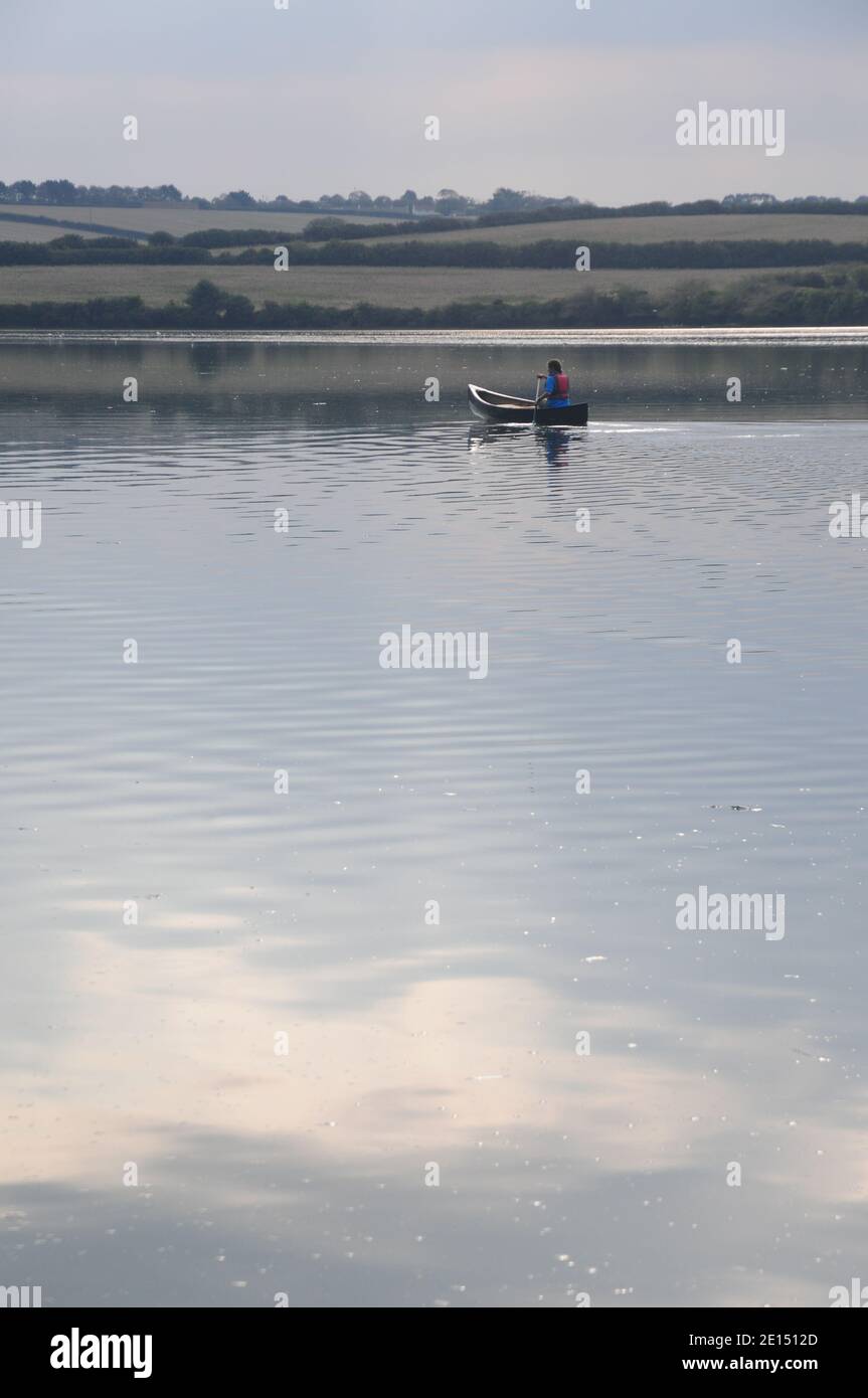 Young lady paddling a Canadian canoe in calm water on a Cornish estuary