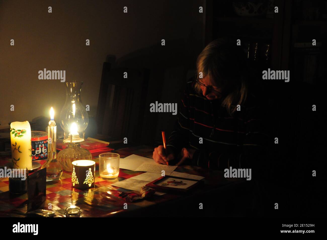 Lady writing Christmas cards at a table by the light of candles and an oil lamp. Stock Photo