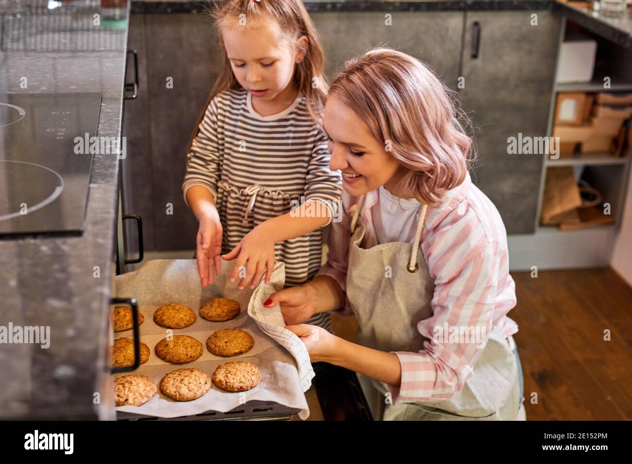 mother and cute kid daughter bake cookies in kitchen, smiling caucasian
