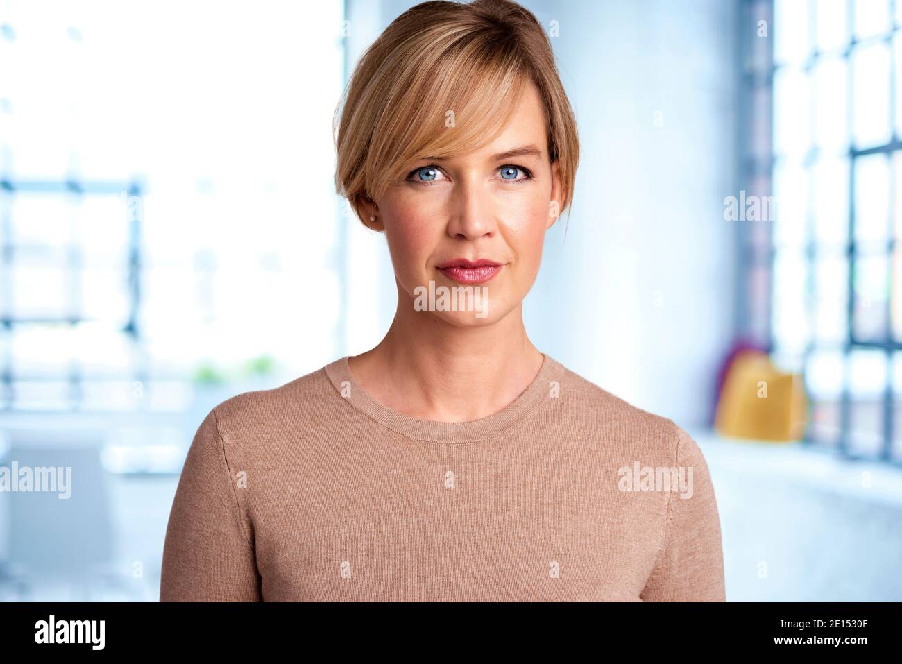 Portrait shot of beautiful blond haired woman looking at camera while standing in the living room at home. Stock Photo