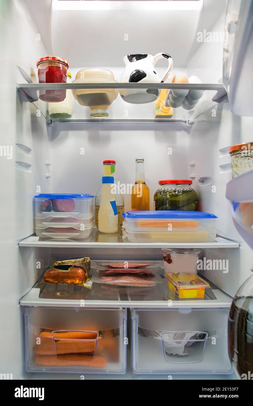 A large refrigerator with lots of food and drink. At the bottom are vegetables and in the middle are sausages and cheese. On top is jam, eggs, milk an Stock Photo