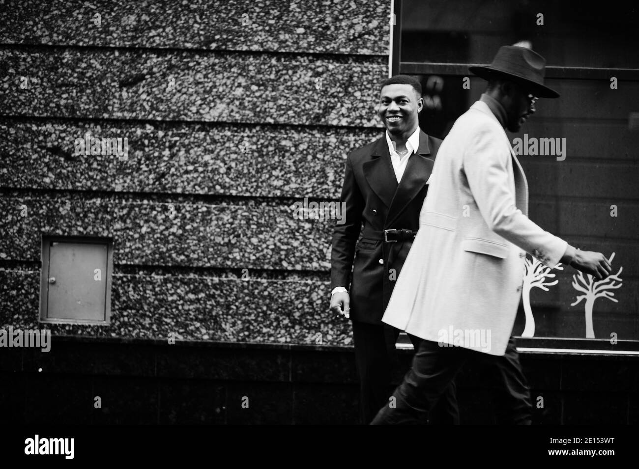 Two fashion black men walking on street. Fashionable portrait of african american male models. Wear suit, coat and hat. Stock Photo
