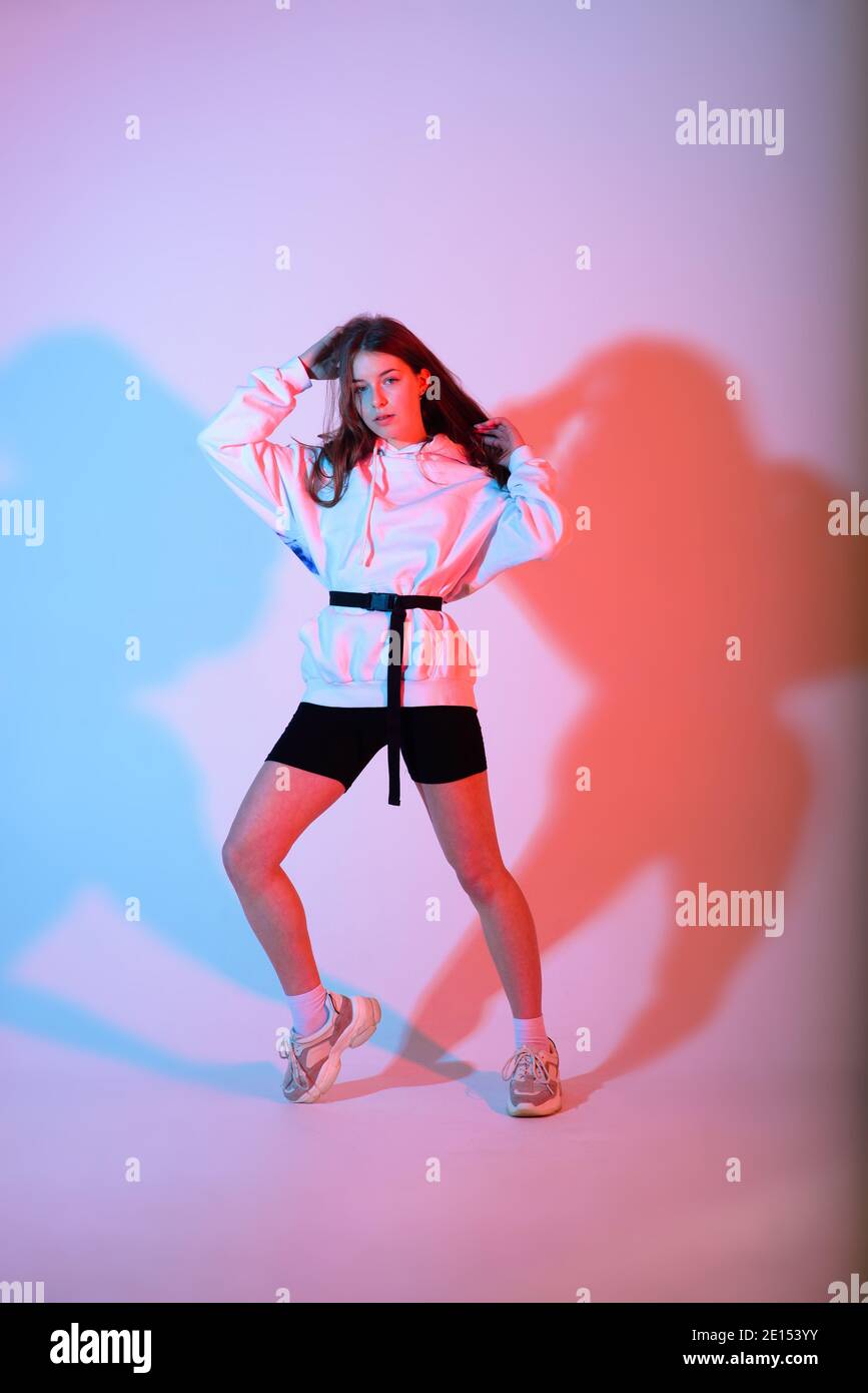 Cute teen girl dancing hip hop in reflective pants, baseball cap, in a  Studio with neon lighting. Dance color poster. Stock Photo