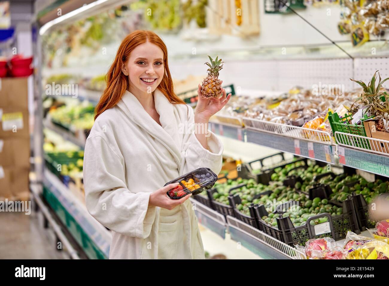 female is choosing fresh vegetables and fruits in the store, wearing bathrobe. young woman