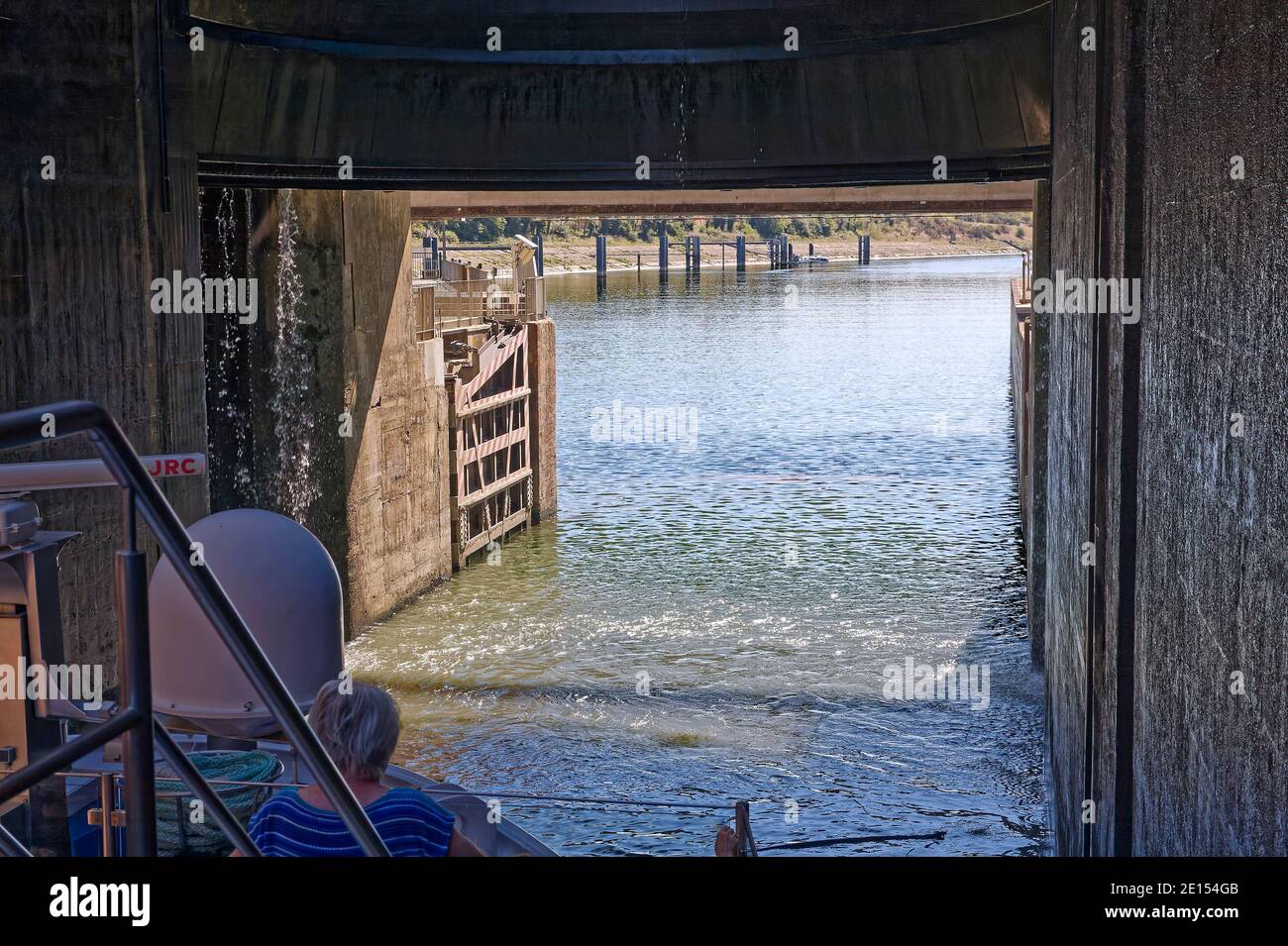 riverboat exiting Bollene Lock, Rhone River, gate up, 71 foot water level difference, engineering feat, travel, transport, narrow, bow, people, Proven Stock Photo