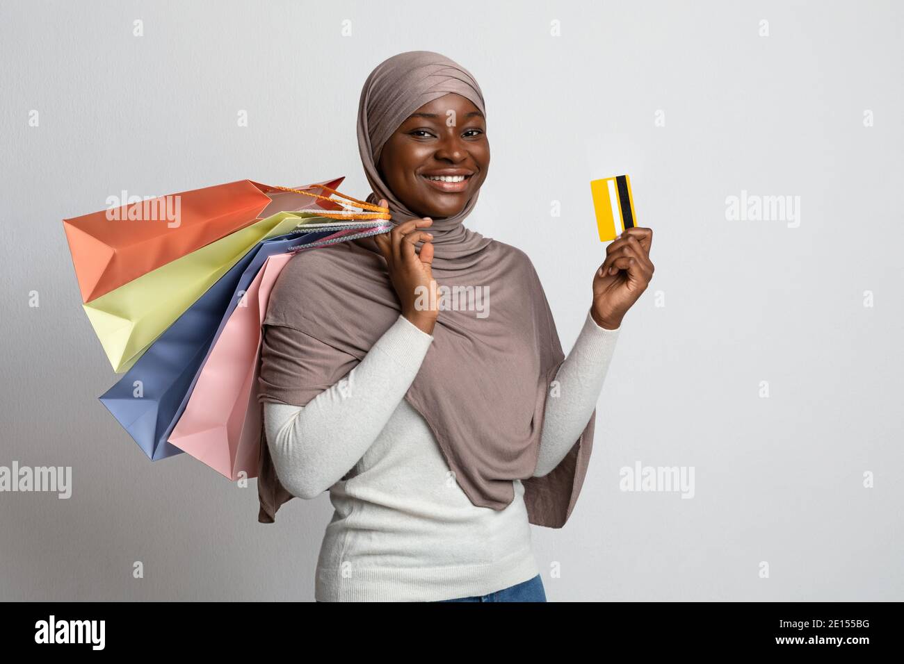 Joyful Black Muslim Shopaholic Woman Posing With Shopping Bags And Credit Card Stock Photo