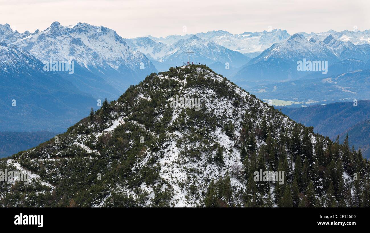 Herzogstand, Germany - Oct 20, 2020: View on Martinskopf mountain. With mountain cross and hikers on top of the mountain. In the back snow-covered alp Stock Photo