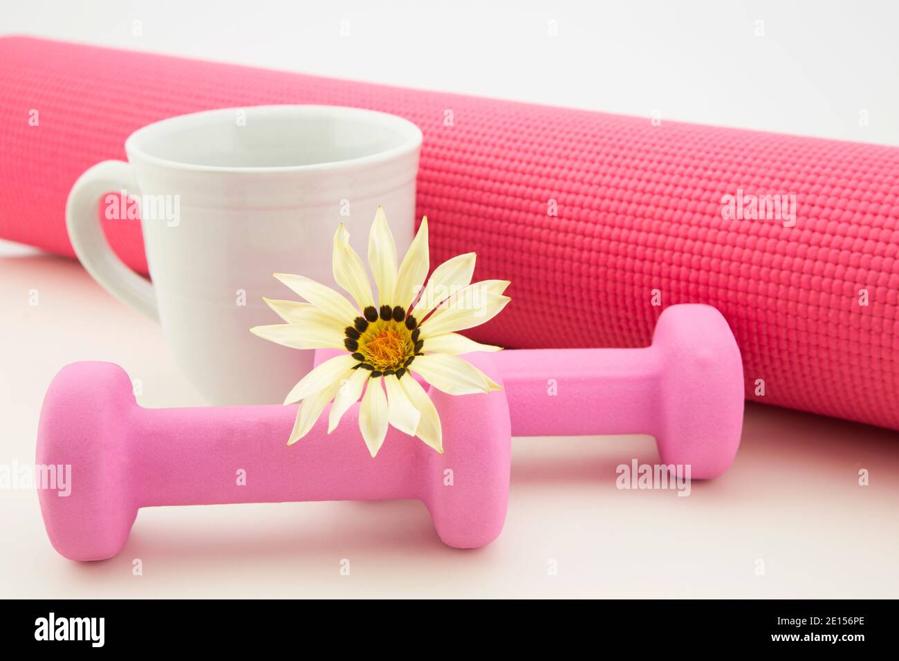 Home fitness portrayed in feminine pink and white hues of yoga mat, mug, flower, and light weights Stock Photo