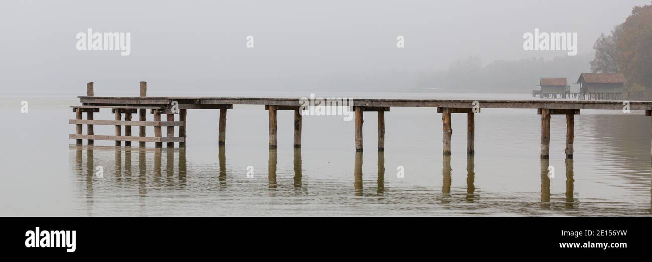 Eching, Germany - Nov 6, 2020: Wooden jetty at Lake Ammersee lduring a foggy autumn day. Panorama format. Stock Photo