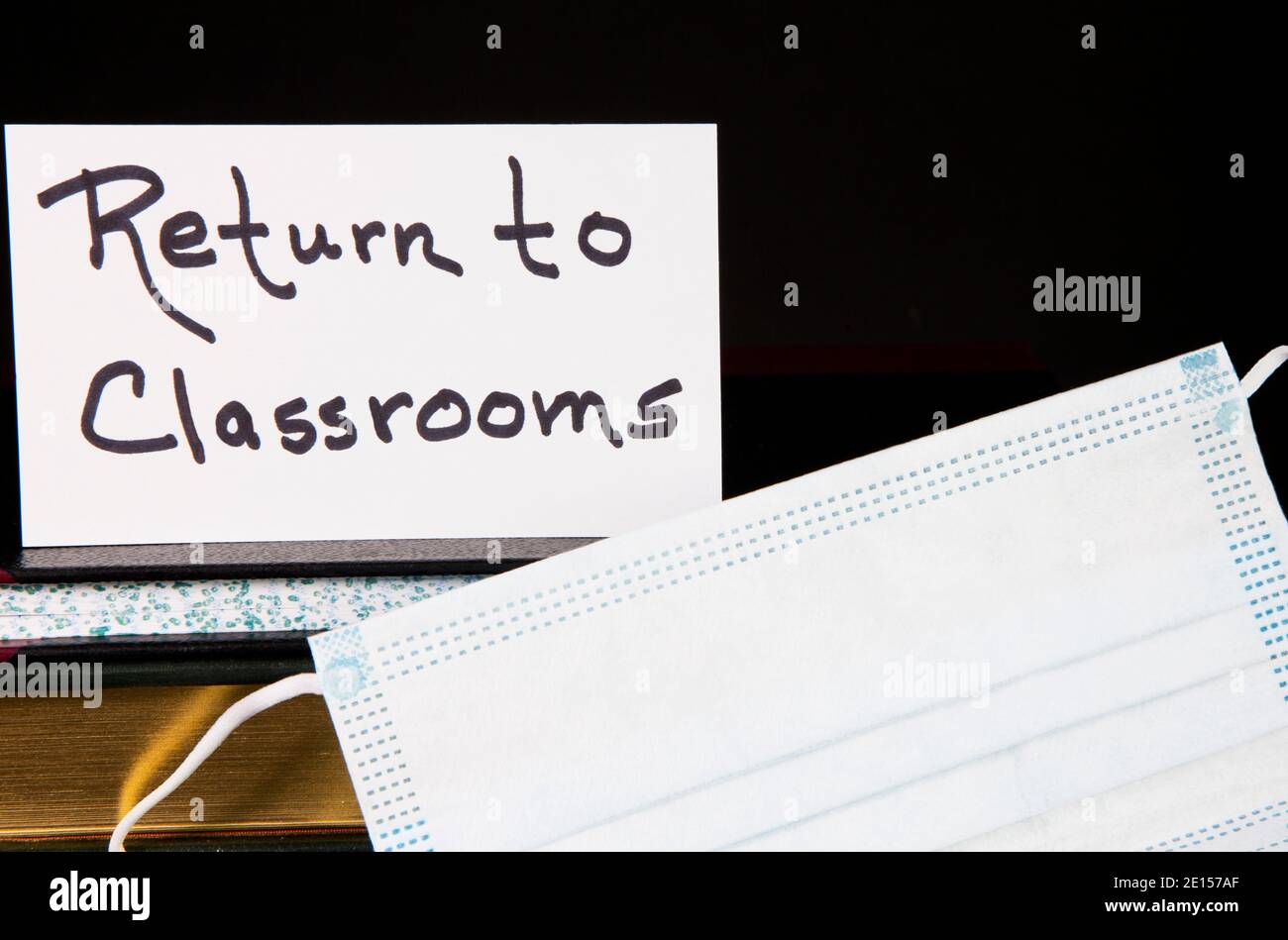 Return to Classrooms note placed with face mask and books reflect public health and education policy needs as schools reopen. Stock Photo