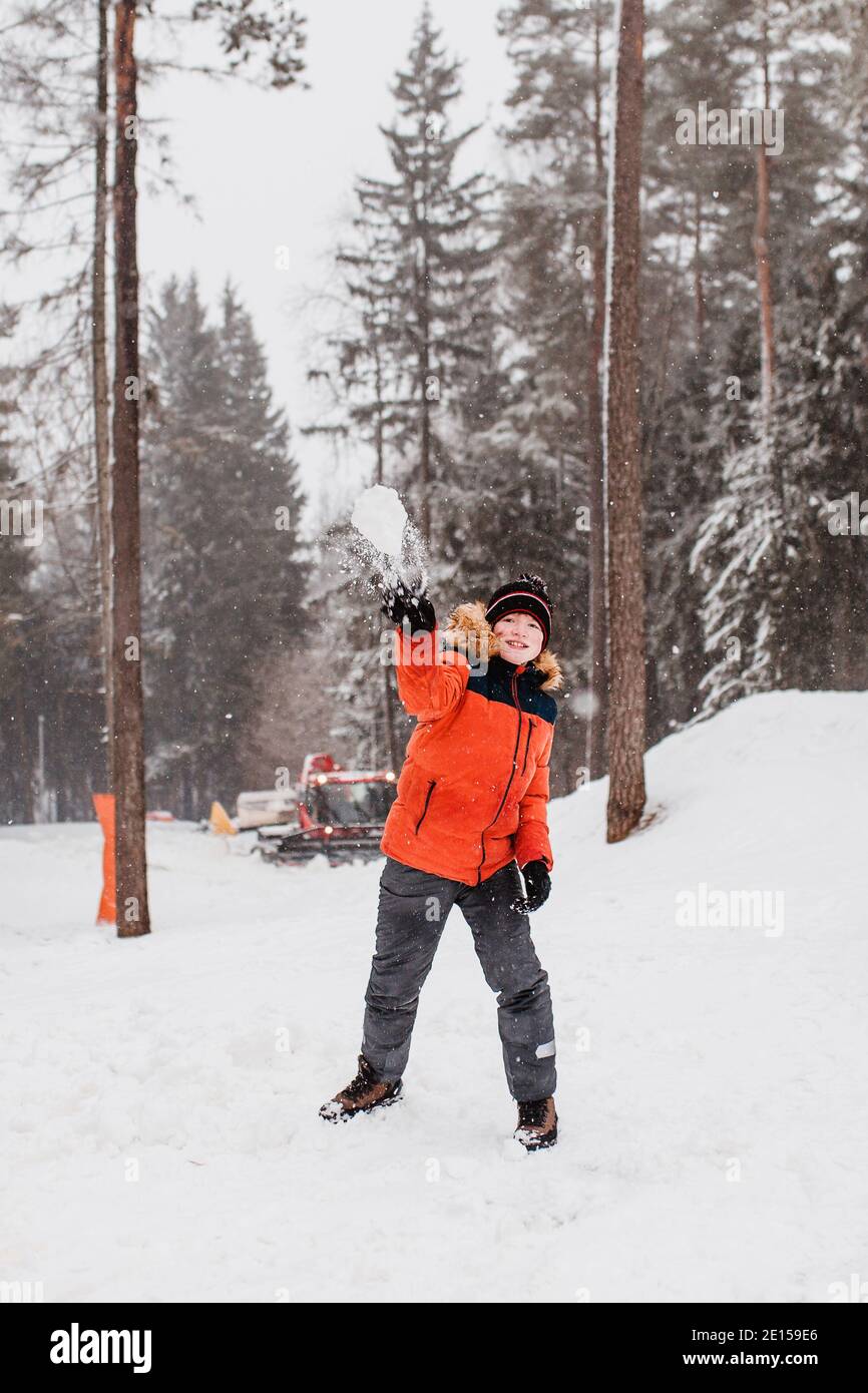 A boy in an orange winter jacket with a hood is having fun in the mountains throwing snowballs - New Year holidays Stock Photo