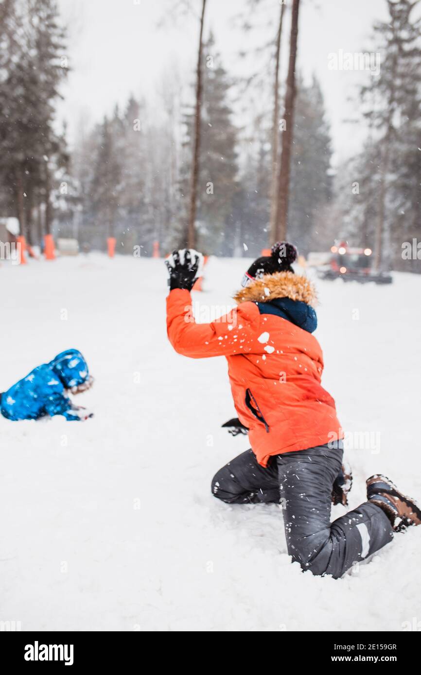 A boy in an orange winter jacket with a hood is having fun in the mountains throwing snowballs - New Year holidays Stock Photo