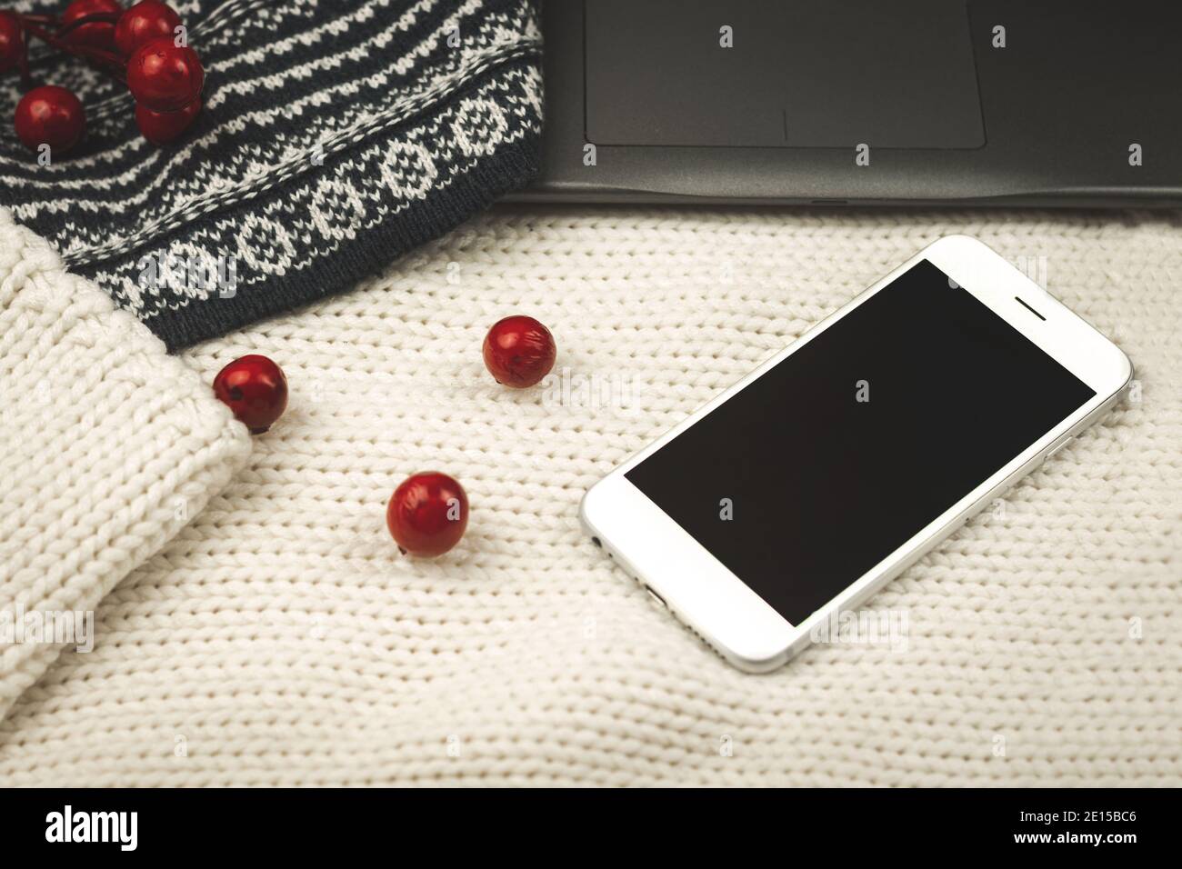 Composition with knitted background, sweaters, decoration and black smartphone, copy space, cozy photo Stock Photo