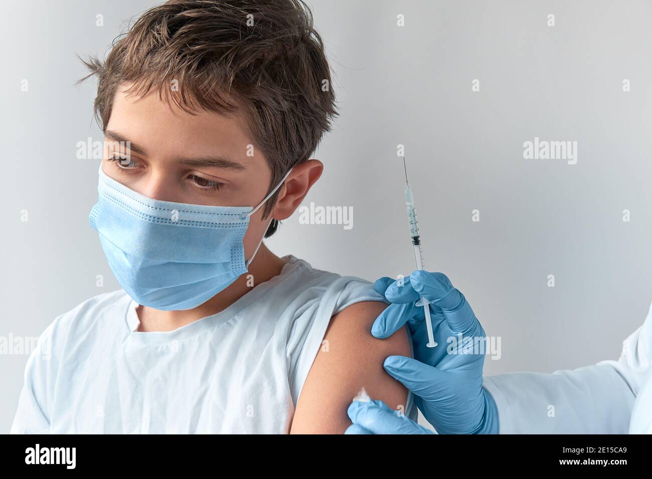 Covid 19, flu or measles vaccination concept. Caucasian teenage boy in face mask, and hand with syringe. Medic, doctor or nurse vaccinates school Stock Photo