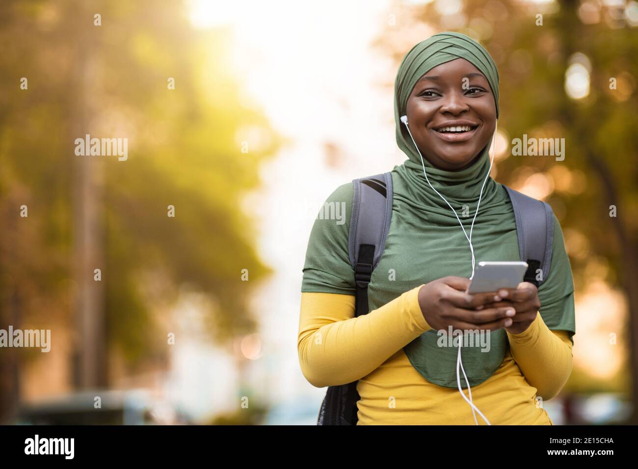Cheerful Black Muslim Lady In Hijab Walking Outdoors Listening Music On ...