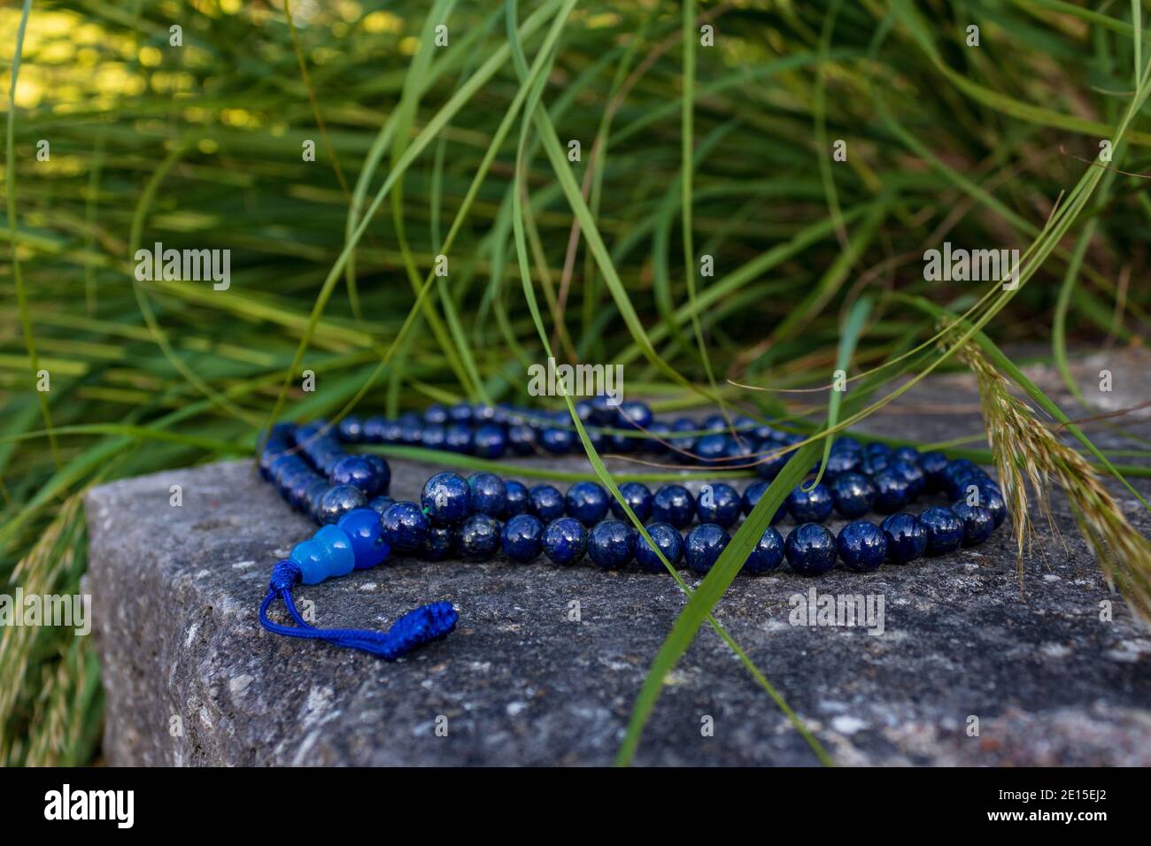 Close up of buddhist prayer beads (Mala) on stone with green grass in the background. Mantra meditation in nature. Stock Photo