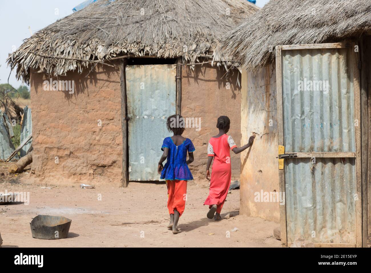 Gambian village children running past mud huts near in a remote village
