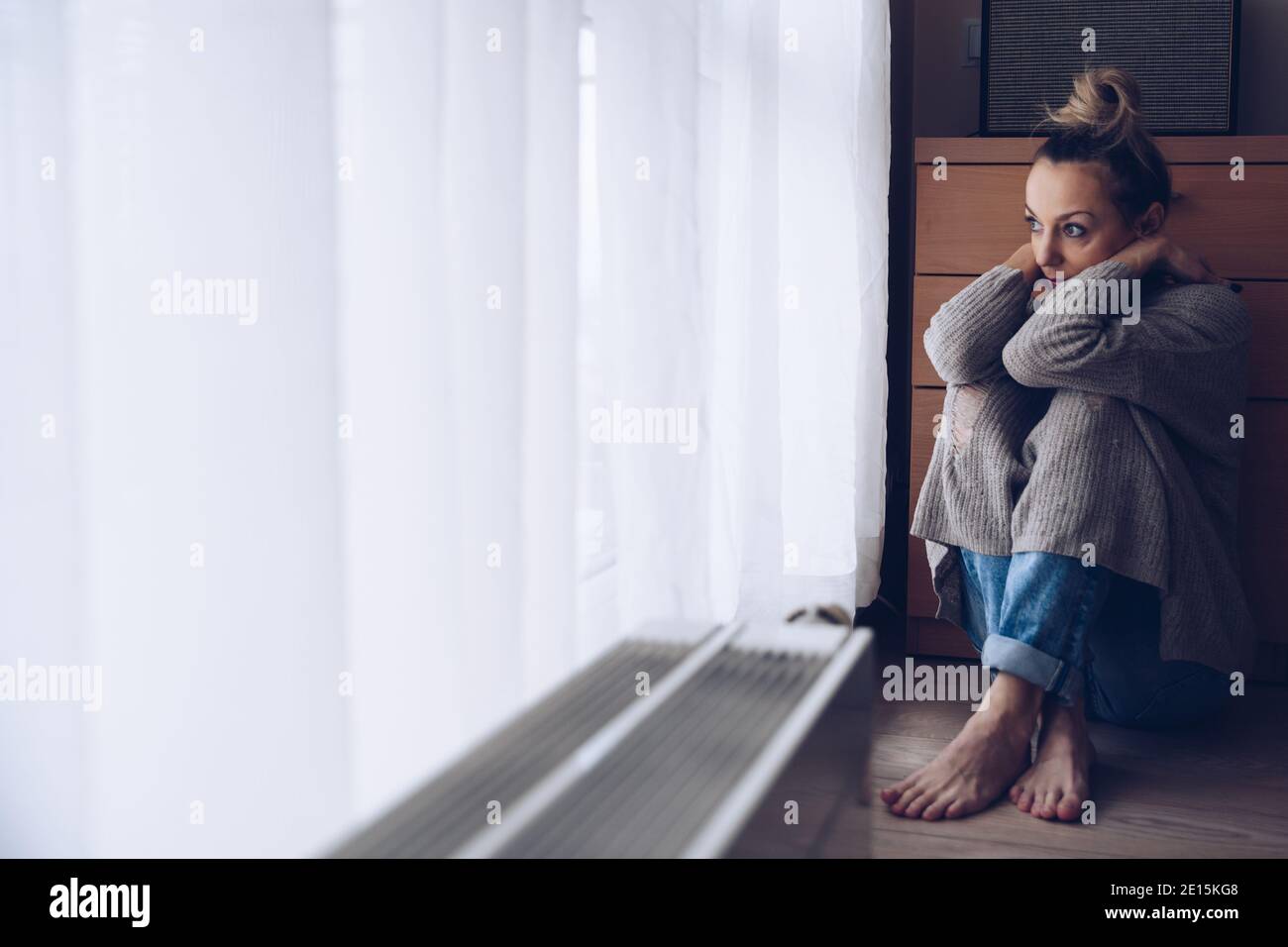 Young sad woman sitting on the floor in her living room looking out the ...