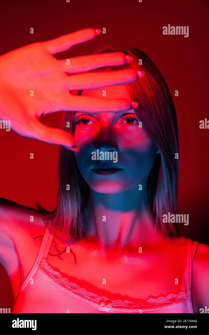 Unemotional young female covering eyes with hand in studio with red light Stock Photo