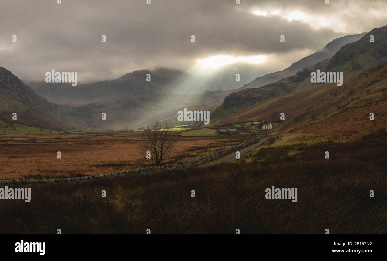 Rays of sunlight piercing the clouds to shine down over Glyderau mountains on the Ogwen Valley landscape in Snowdonia, North Wales UK Britain. Stock Photo