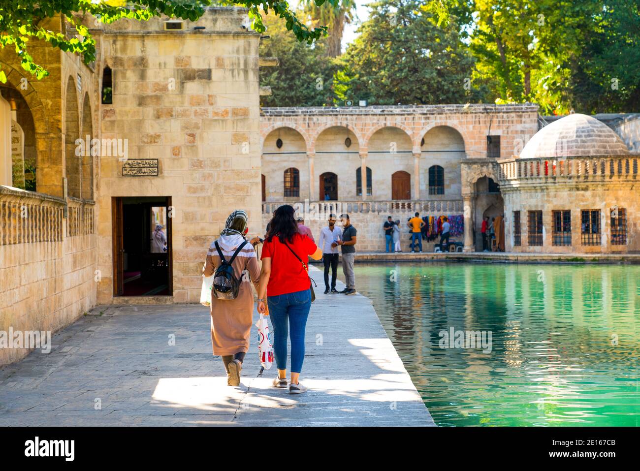 Sanli Urfa, Turkey: September 12 2020: Rear view of two female tourists near Pool of Abraham (Balikli Gol) and historic buildings in background Stock Photo