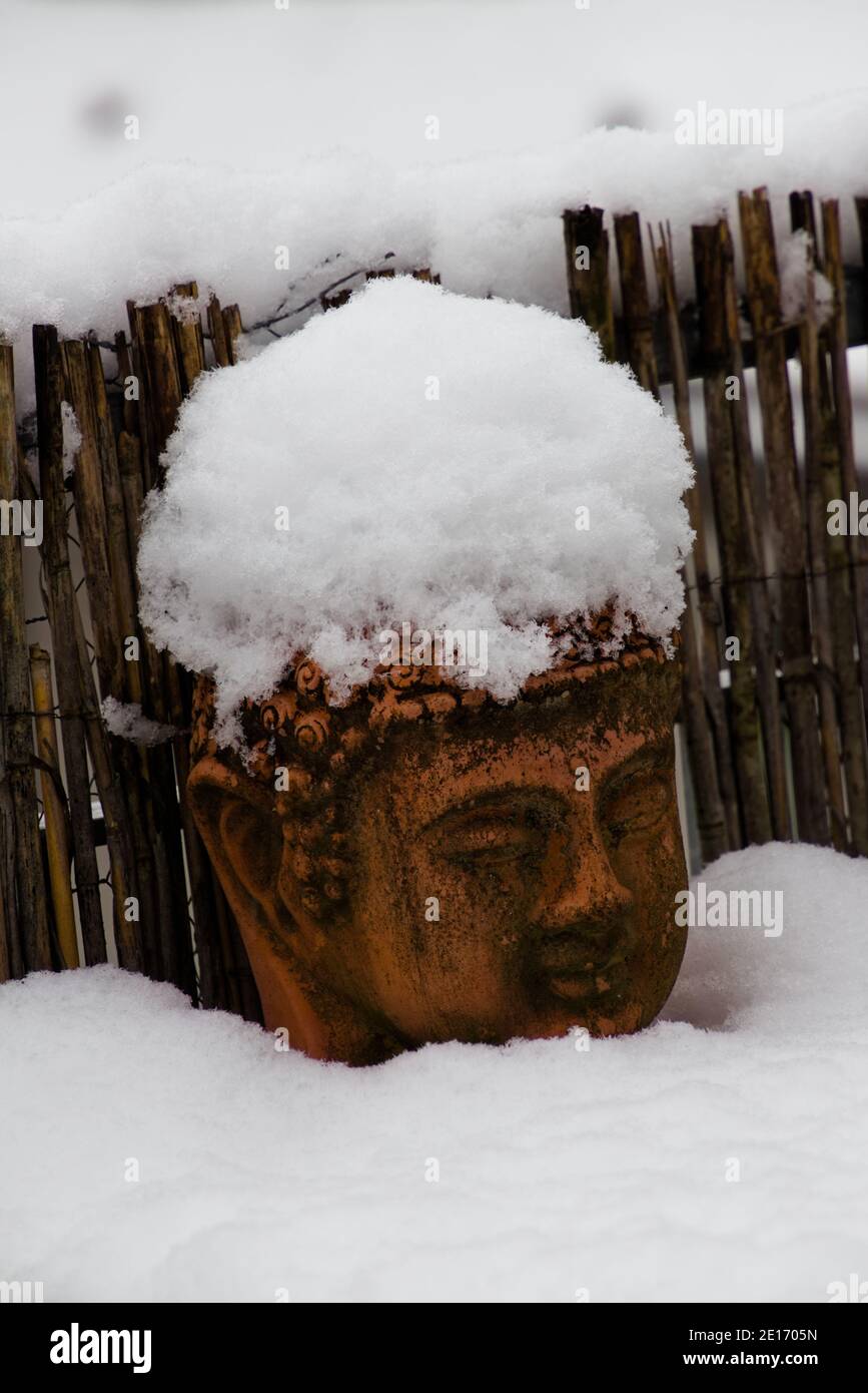 Old weathered terracotta buddha head covered with snow Stock Photo