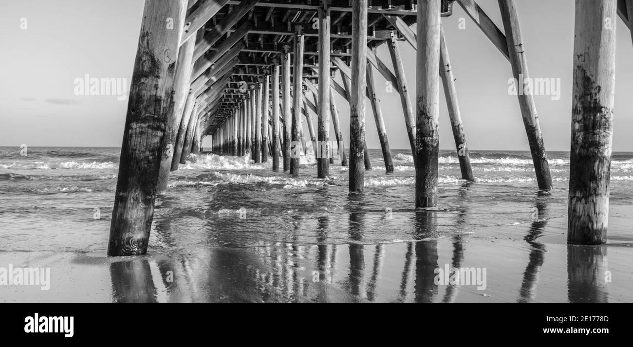 Under The Boardwalk. Black and white ocean pier on the coast of the Atlantic Ocean on a sunny summer day in Myrtle Beach, South Carolina, USA. Stock Photo