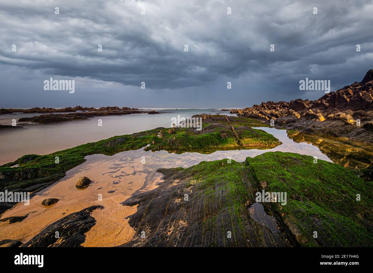 Stone with moss and rugged rocks with small pools of water on Almograve beach Stock Photo