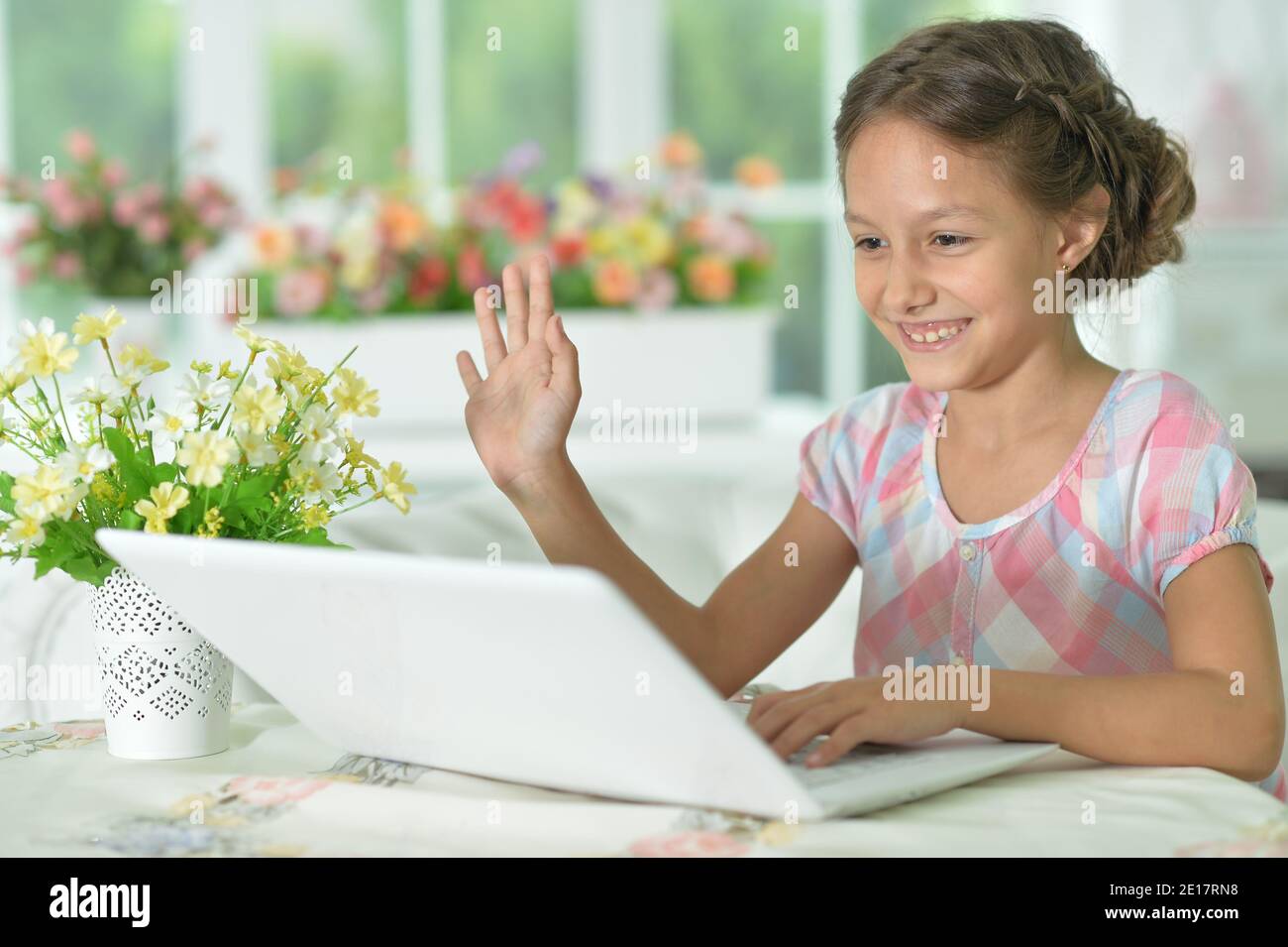 Emotional cute girl using laptop at home waving hand Stock Photo - Alamy