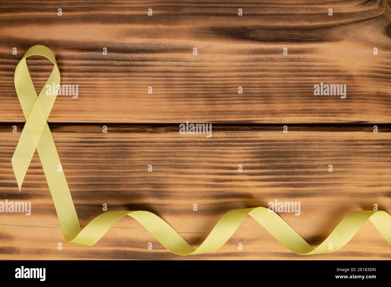 Yellow awareness ribbon, on wooden background. Sarcoma. Childhood cancer. World Cancer Day. Flat lay. Copy space Stock Photo