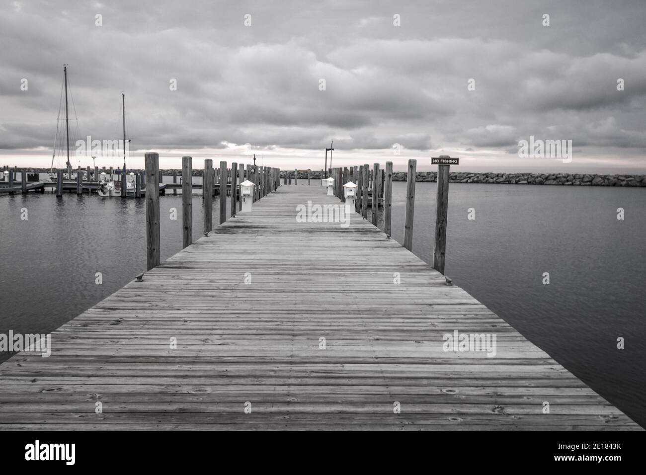 Moody black and white landscape of a boardwalk pier extends to the horizon on the Great Lakes coast of Michigan on a cloudy overcast day. Stock Photo