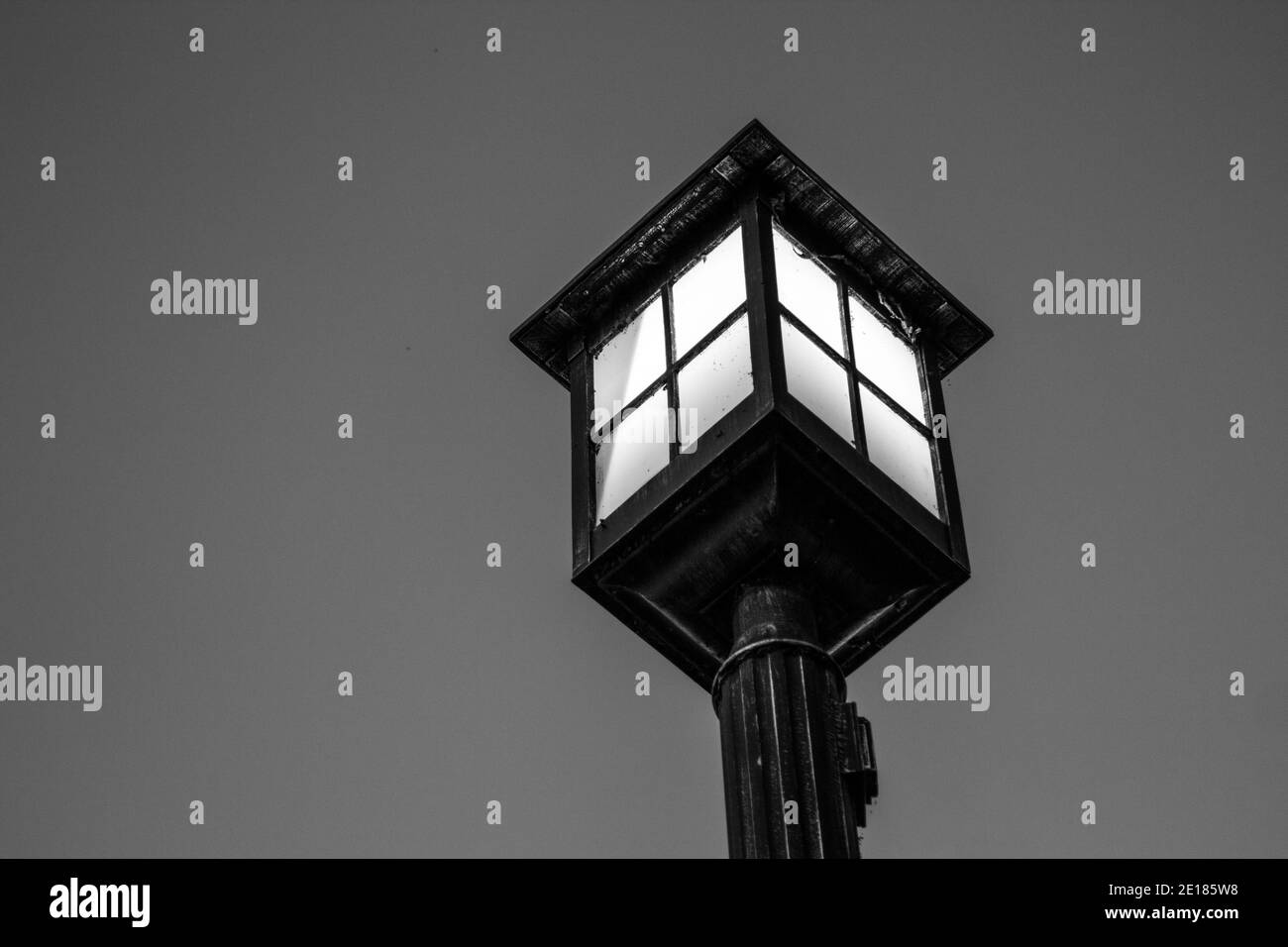 Old fashioned lamp post illuminated against the night sky. Black and white in horizontal orientation with copy space. Stock Photo