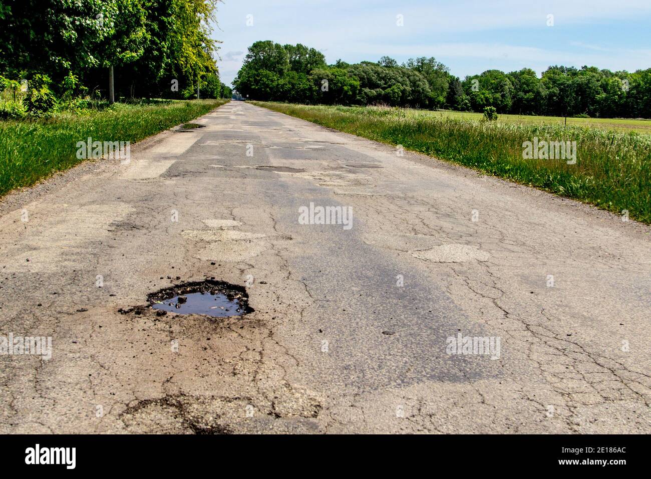 Terrible Michigan Roads. Rural two lane paved road with huge pothole, cracked aging asphalt and no lines painted on the pavement. Stock Photo