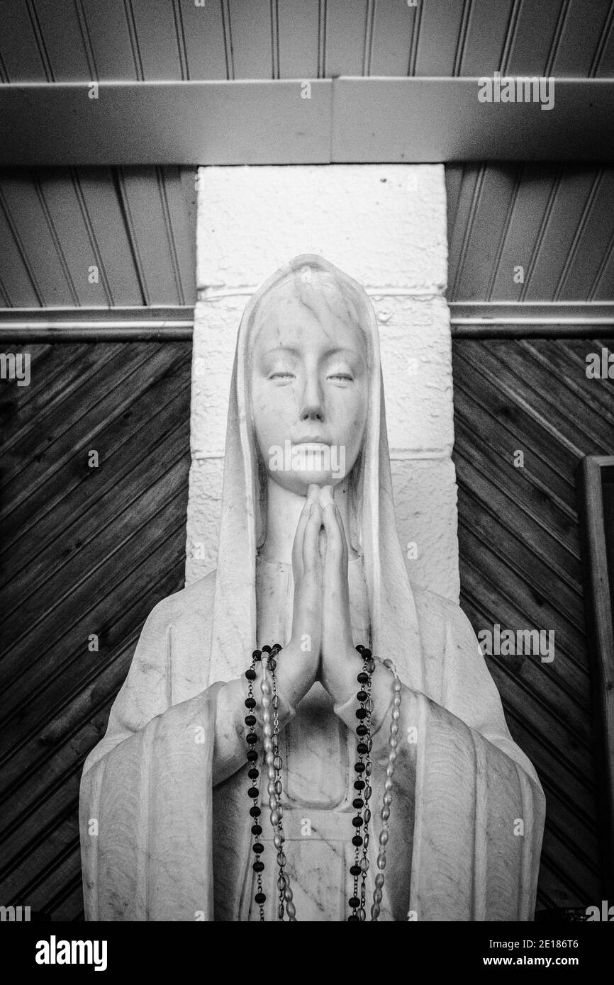 The Virgin Mary. Statue of the Virgin Mary praying with rosary beads in her hands. Black and white in vertical orientation. Stock Photo