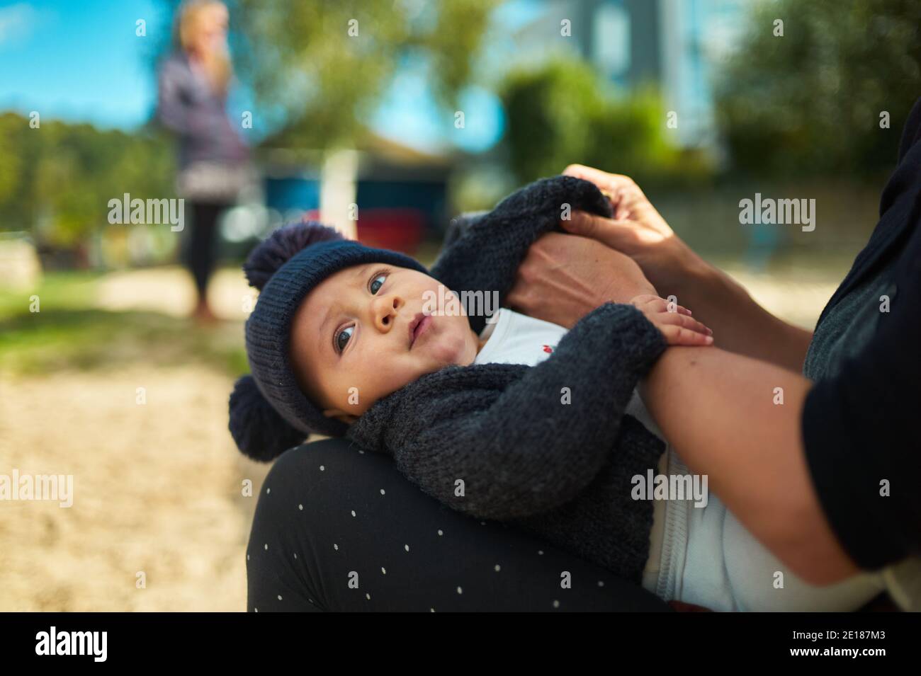 A little baby is resting in his mothers lap on a sunny autumn day in the park Stock Photo