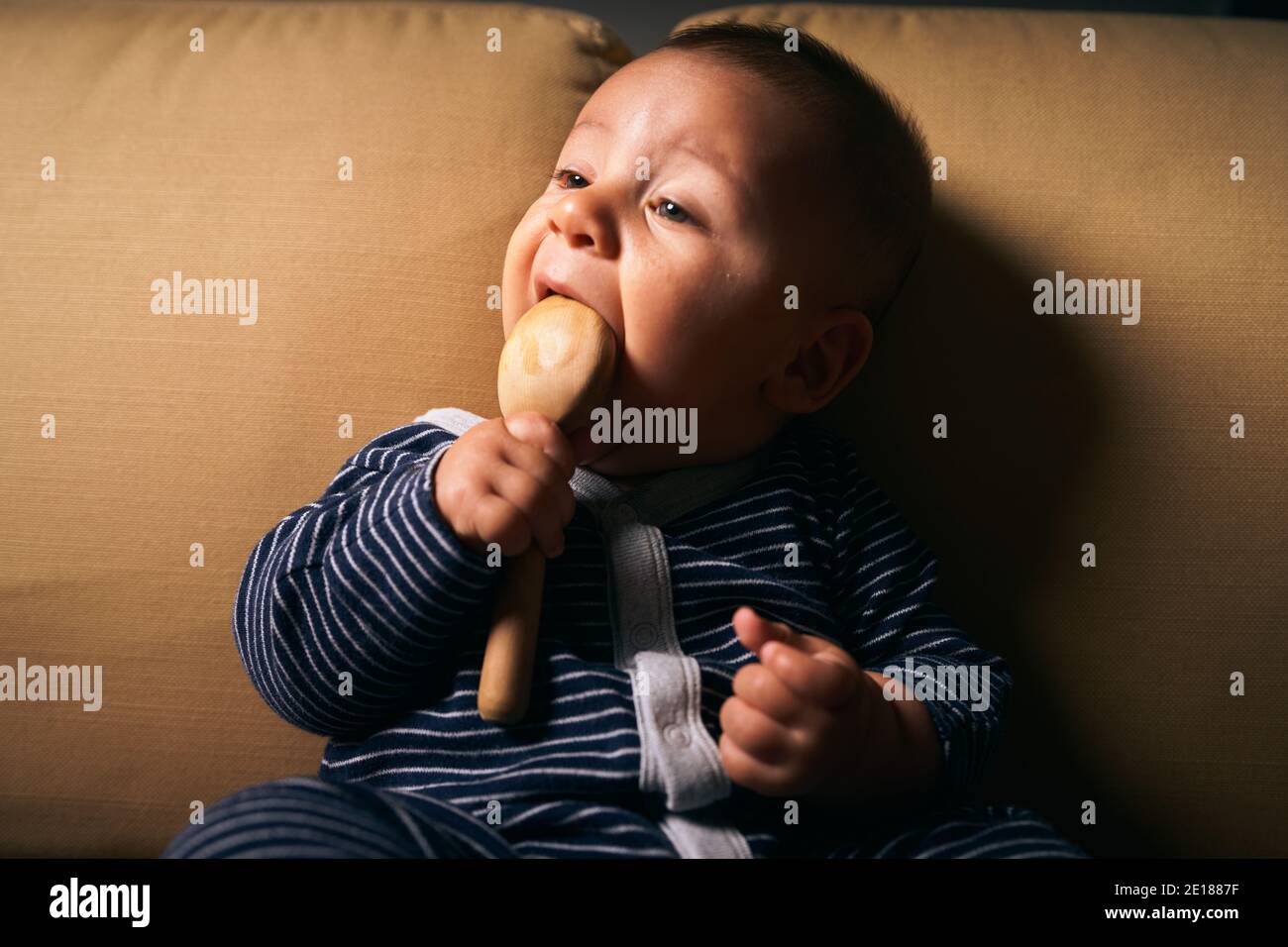 A little baby with a wooden rattle is sitting on a sofa Stock Photo Alamy