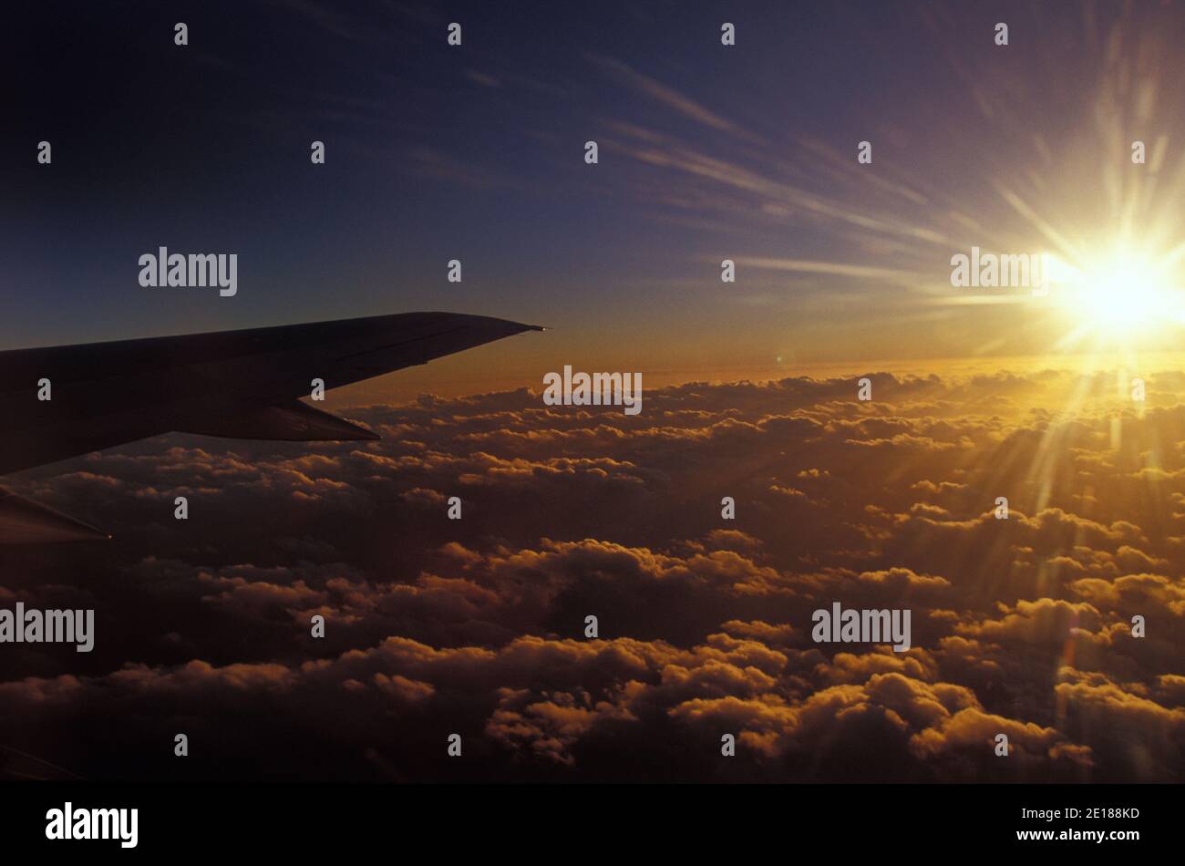 Sunset over clouds seen from airplane with wing in frame Stock Photo
