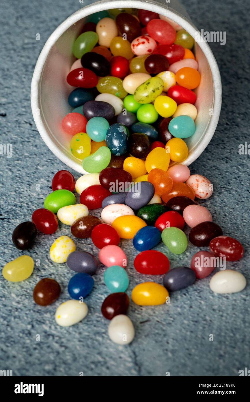Jelly beans spilling from white foam cup against blue background table ...