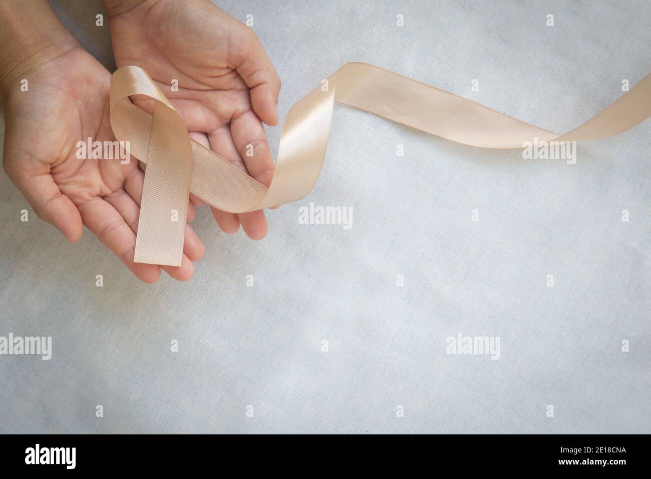 Hands holding gold ribbon on white fabric background with copy space. The international awareness symbol for Childhood Cancer. World Cancer Day. Healt Stock Photo