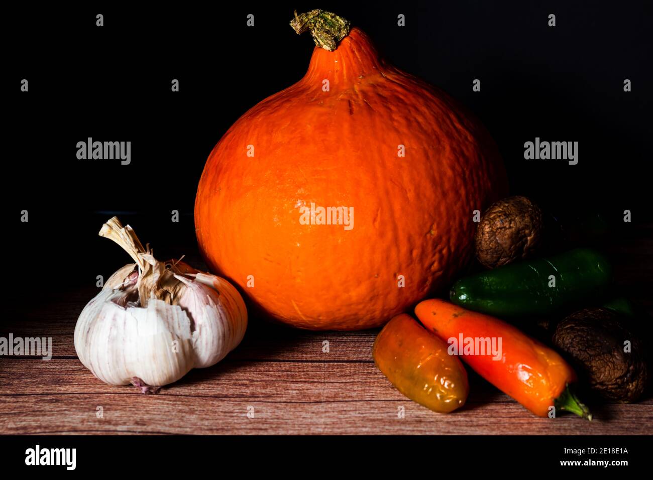 Uchiki Kuri or Red Kuri squash with peppers and garlic in a still life. Natural nutrition concept. Stock Photo
